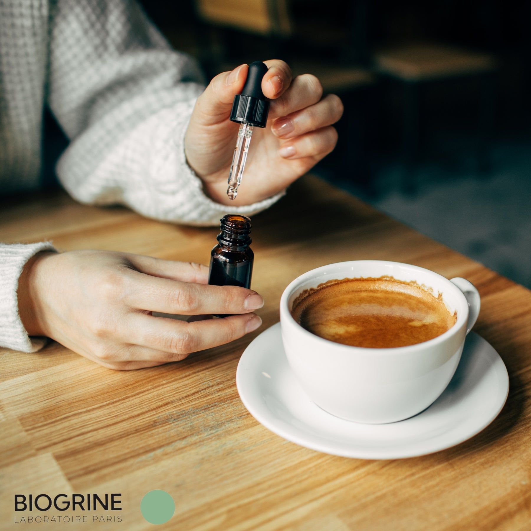 Mani che tengono una bottiglia marrone e un contagocce sopra una tazza di caffè.