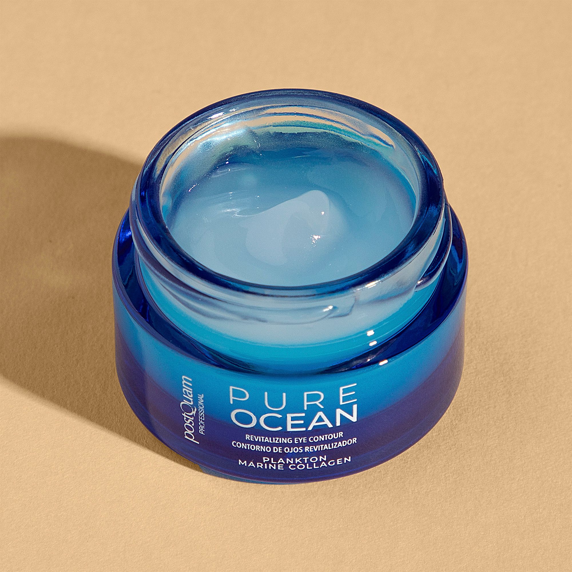 Vasetto aperto con crema per occhi. Vasetto di vetro blu con coperchio bianco. Testo: Pure Ocean, Revitalizing Eye Contour, Plankto Marine Collagen. PostQuam.