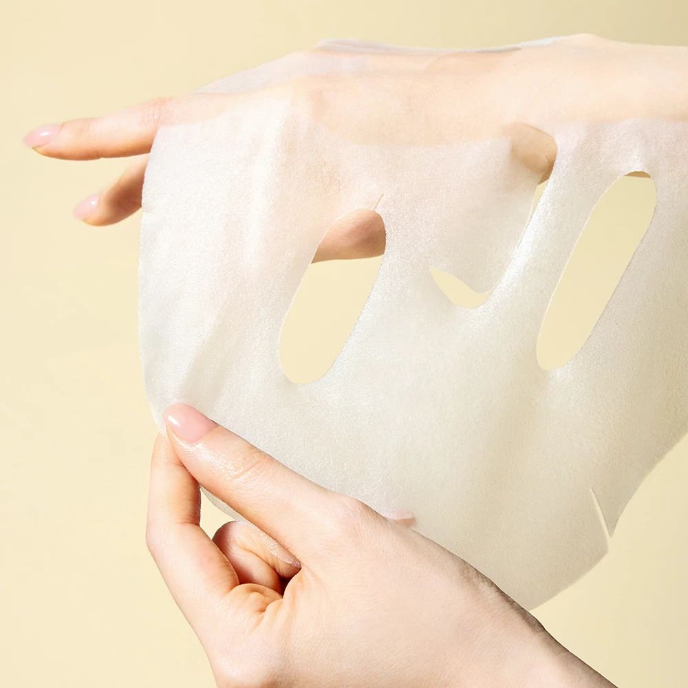 Mani che tengono una maschera facciale bianca con aperture per occhi e bocca.