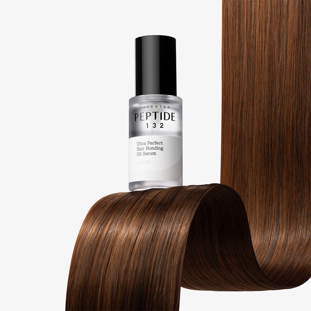 Siero oleoso COSRX Peptide 132 Ultra Perfect Hair Bonding in flacone di vetro su capelli ondulati.