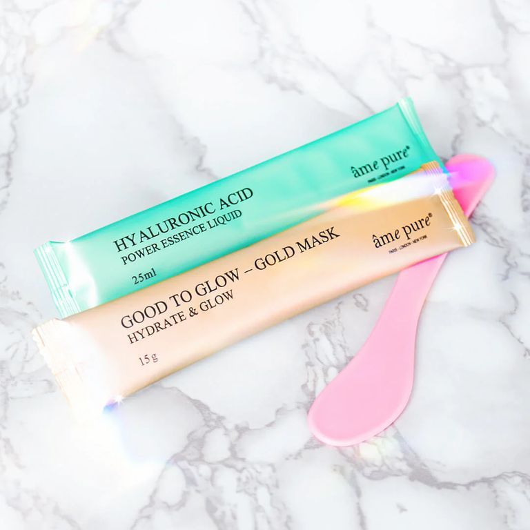 Due bustine di maschera e una spatola. Verde e oro. Testo: âme pure, Hyaluronic Acid, Good to Glow. Su marmo bianco.