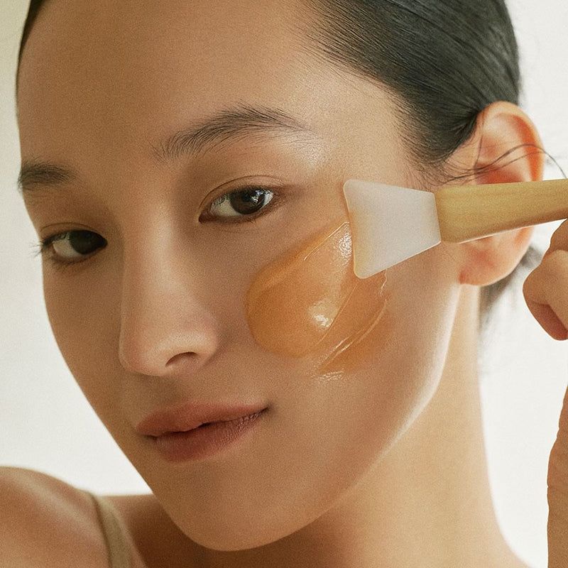 Persona applica maschera al miele sul viso con spatola. Primo piano.