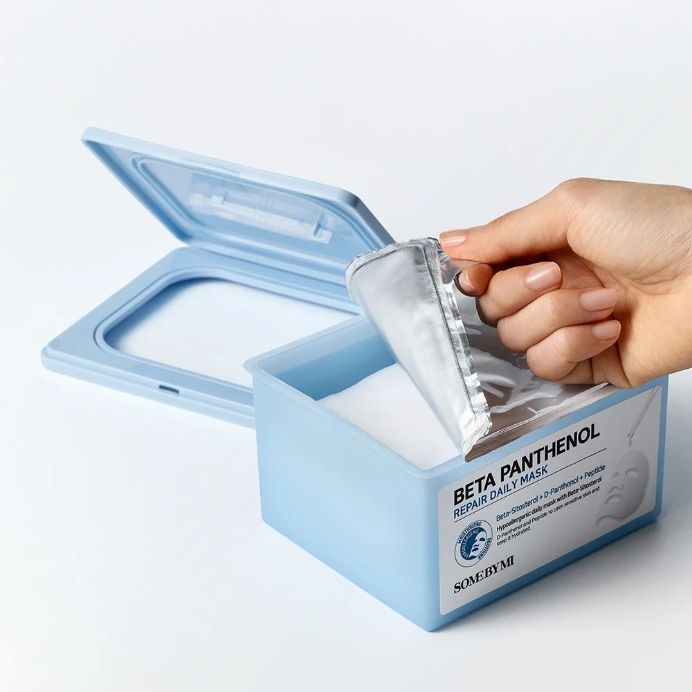 Scatola blu con coperchio, mano estrae maschera. Scritta: Beta Panthenol Repair Daily Mask. Logo SOME BY MI.