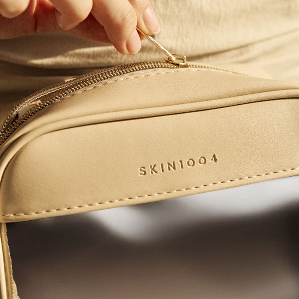 Primo piano di una pochette cosmetica beige. Cerniera in apertura. Logo SKIN1004 visibile.