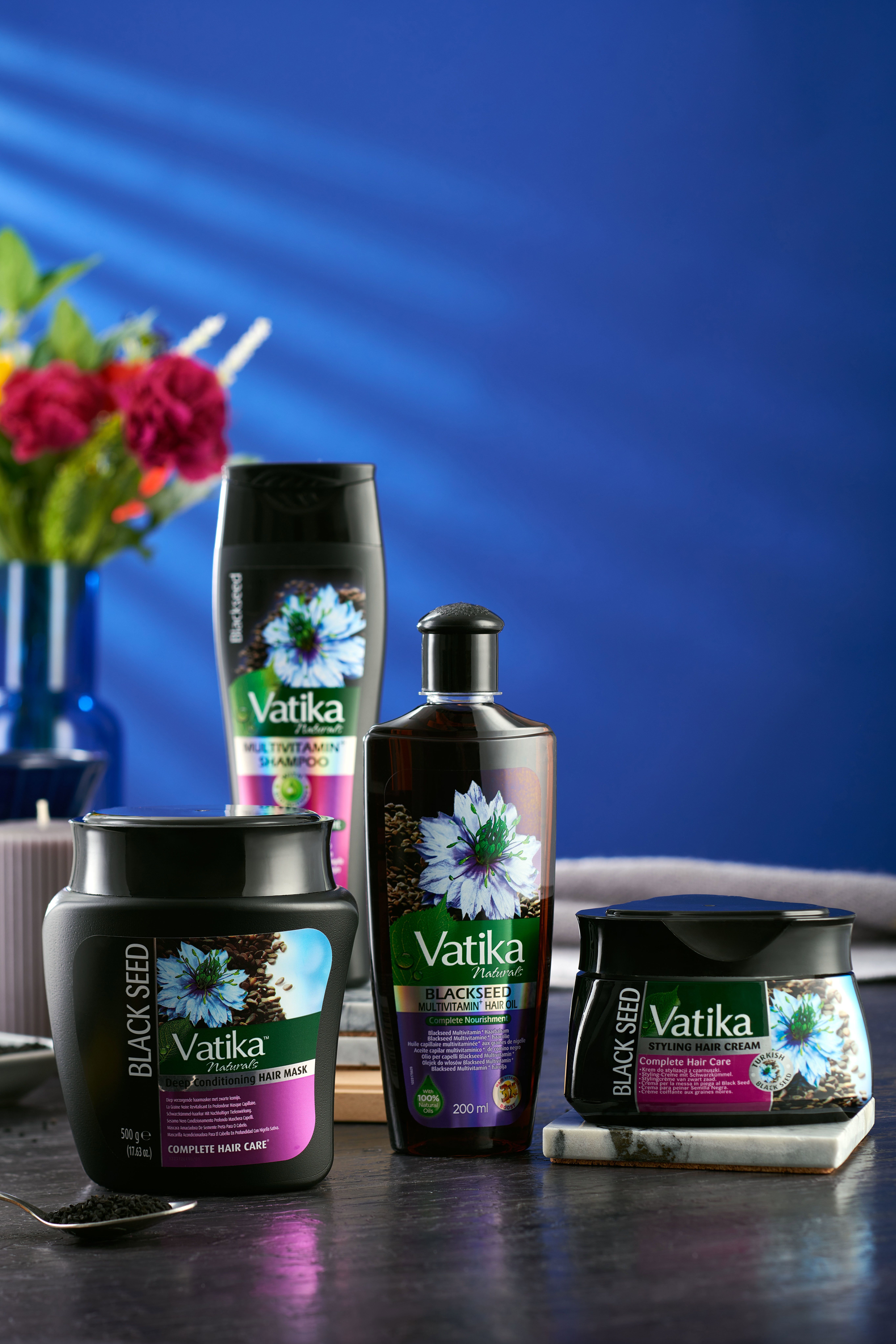 Set di prodotti: maschera per capelli, shampoo, olio e crema. Confezioni nere con logo Vatika e illustrazione di semi di cumino nero. Su un tavolo.