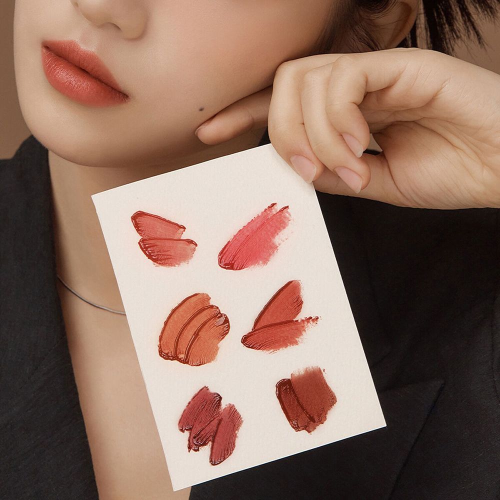 Persona che tiene una scheda con campioni di lucidalabbra. Diverse tonalità sono visibili.