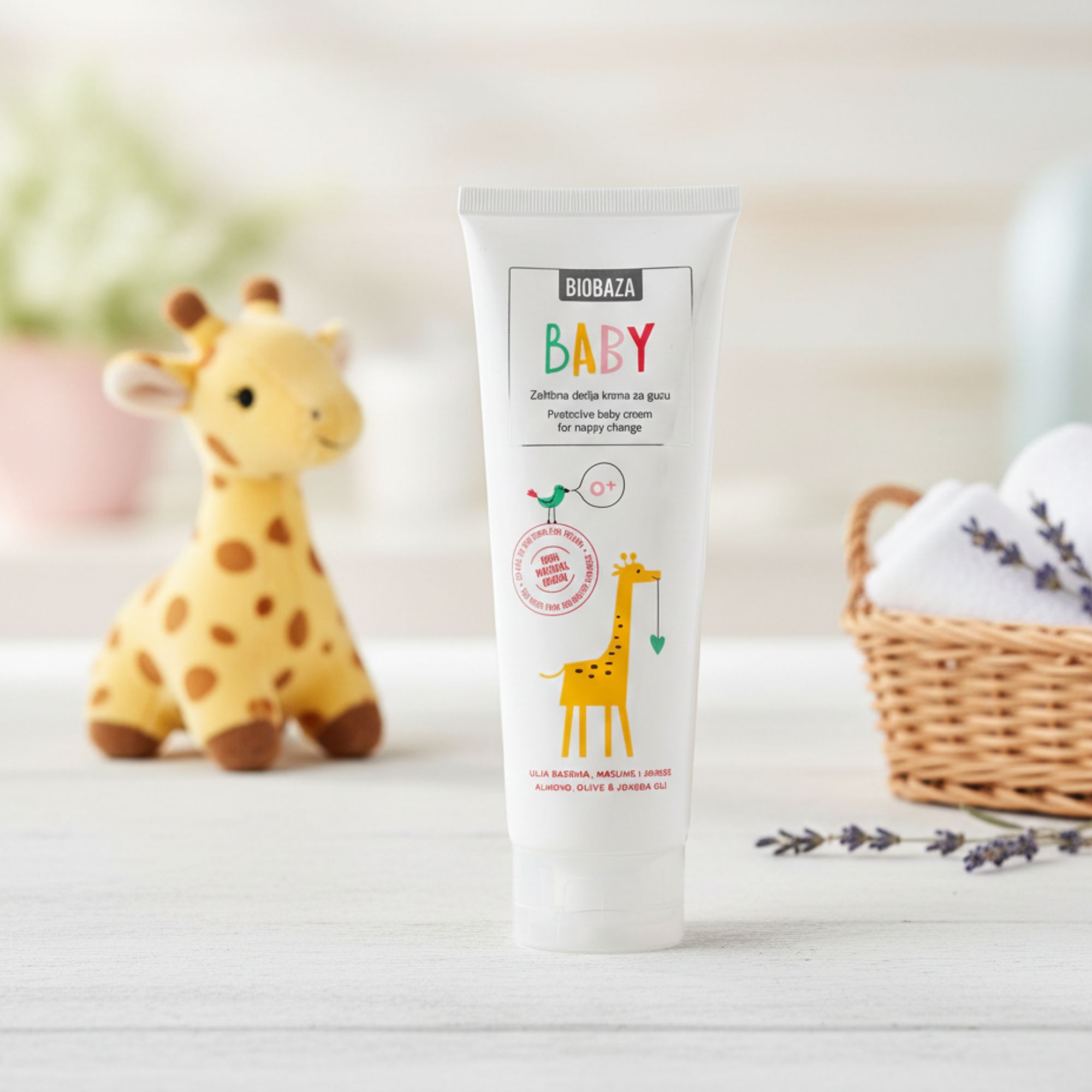 Tubo bianco con scritta BABY e illustrazione di una giraffa. Si trova accanto a un peluche e a un cestino con asciugamani.