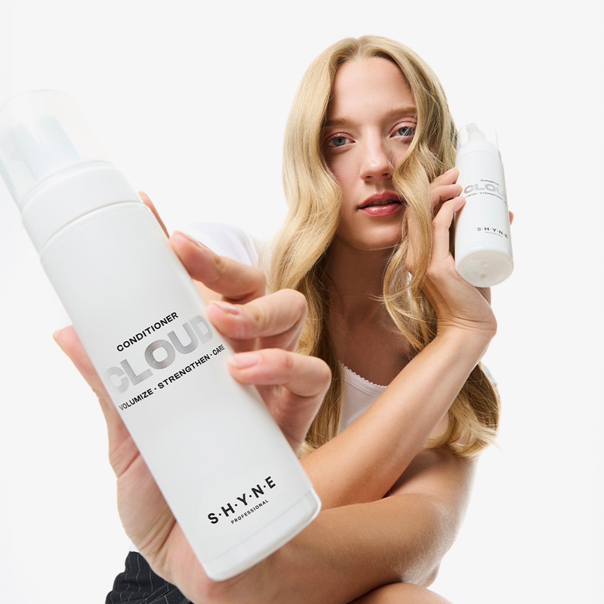 Donna tiene due flaconi bianchi. Uno reca la scritta "CONDITIONER CLOUD" e "S.H.Y.N.E".