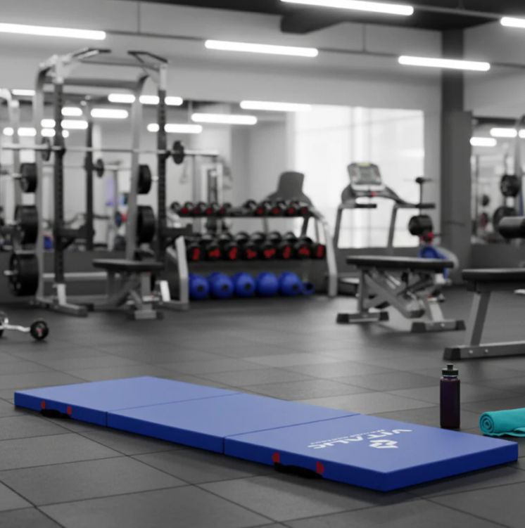 Tappetino yoga blu in palestra. Logo VITALIC. Attrezzi per il fitness sullo sfondo. Asciugamano e bottiglia.