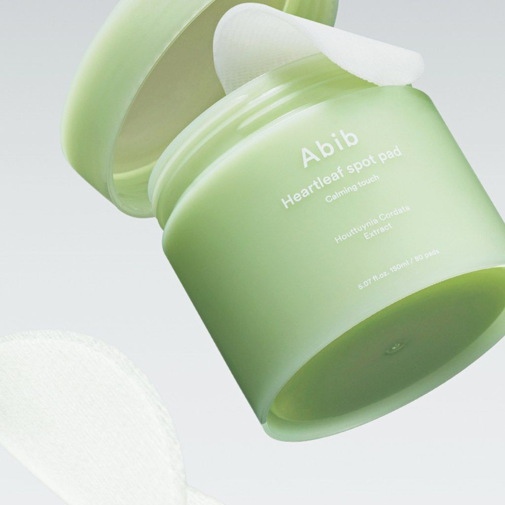Contenitore verde, coperchio aperto, pad visibile. Scritta: Abib Heartleaf spot pad. Testo sottostante: Calming touch, Houttuynia Cordata Extract.