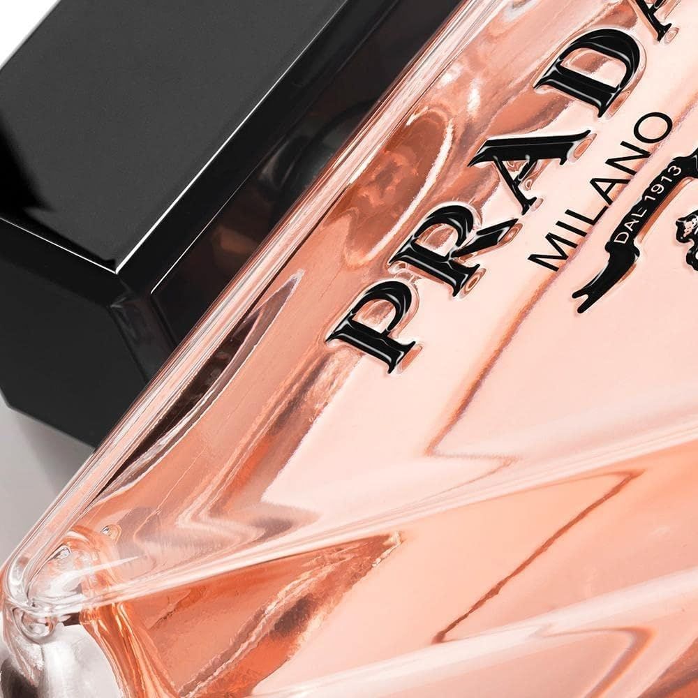 Primo piano del flacone. Forma triangolare, liquido rosa, tappo nero. Scritta: Prada Milano.