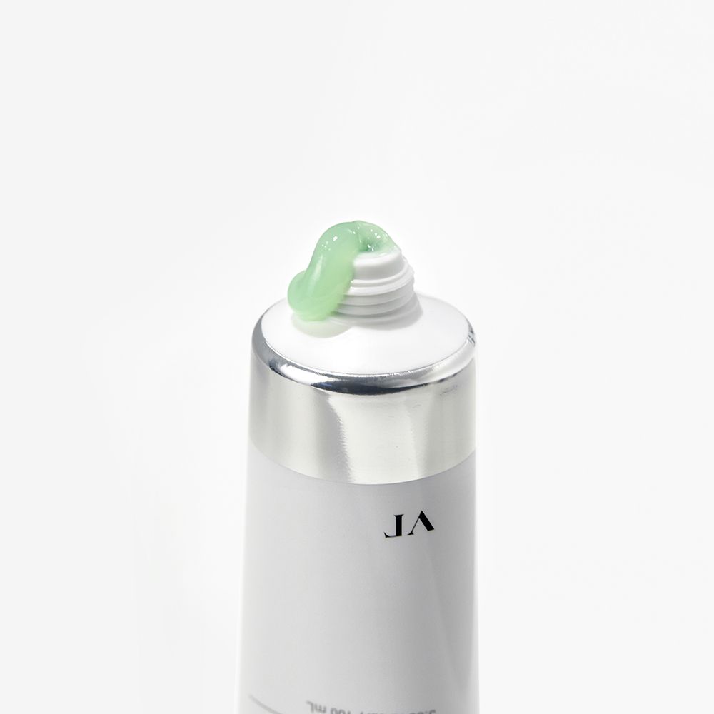 Primo piano di un tubo. Tubo bianco con tappo argentato, crema verde che esce dall'apertura.
