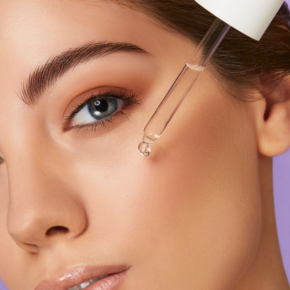 Primo piano: goccia di siero sul viso. Pipetta. Pelle. Sfondo: viola.