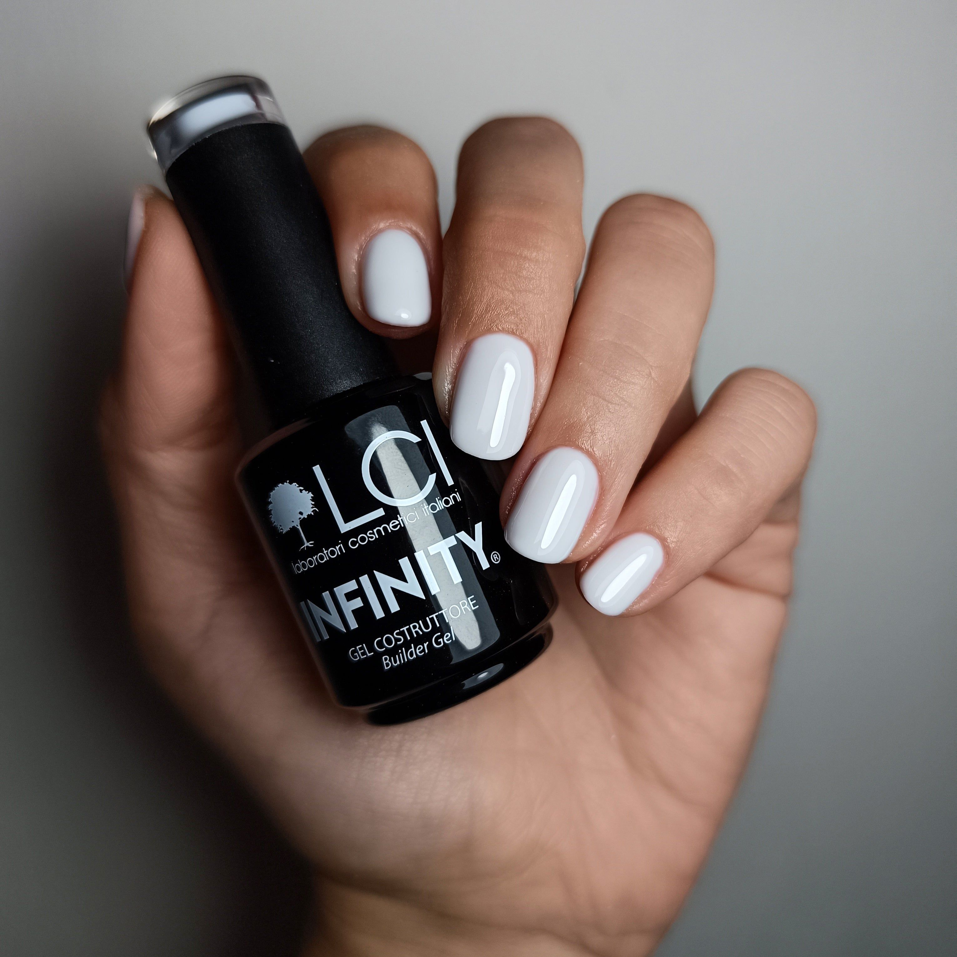 Mano con unghie smaltate e flacone. Unghie smaltate con gel bianco. Flacone: LCI INFINITY Builder Gel.