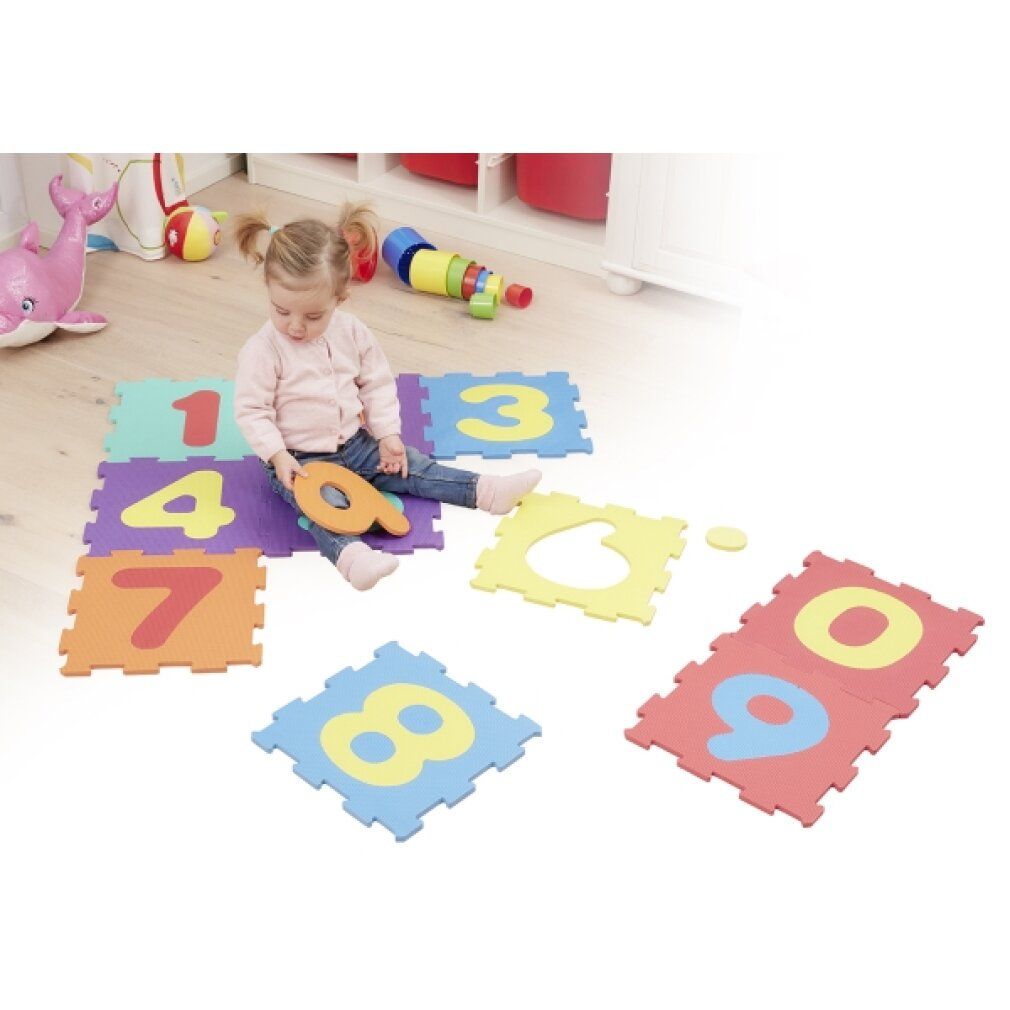 Bambino seduto su tappetini puzzle con numeri. Colori diversi. Singoli pezzi di puzzle sparsi. Numero 9 tenuto in mano.