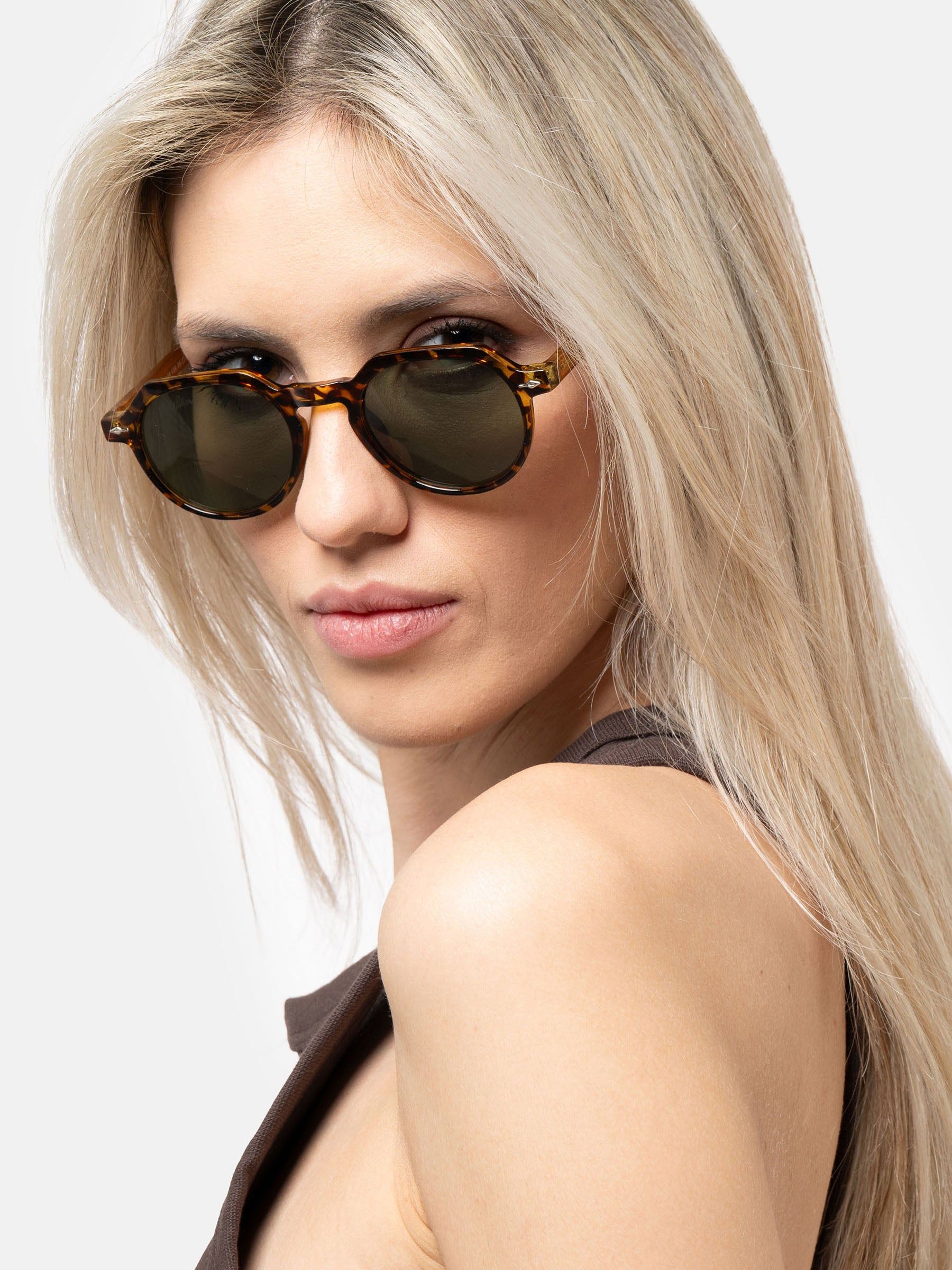 Donna con occhiali da sole. Montatura marrone, lenti verdi. Logo Herling sulla lente. Primo piano.