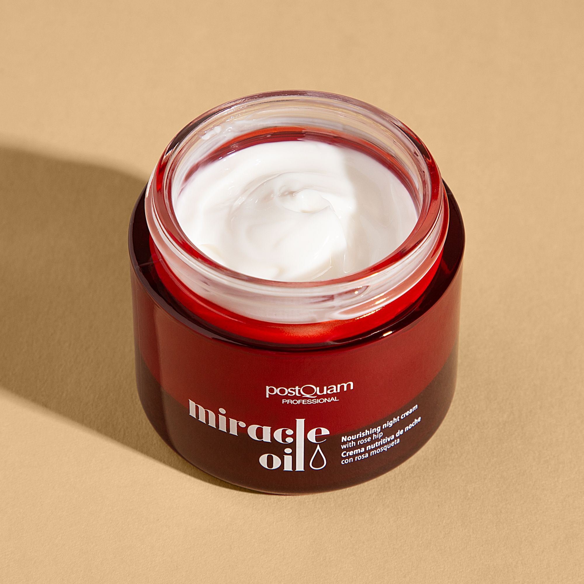 Vaso rosso aperto con crema bianca. Scritta: "postQuam PROFESSIONAL miracle oil". Testo: "Nourishing night cream with rose hip".