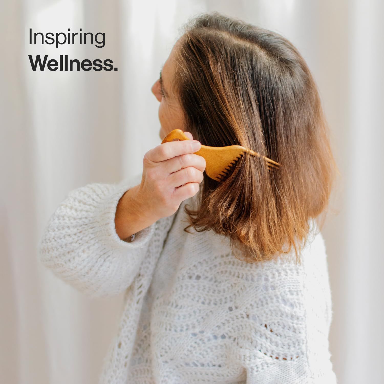 Una donna si pettina i capelli con un pettine di legno. Il pettine ha dei denti e un manico. La donna indossa un maglione bianco.