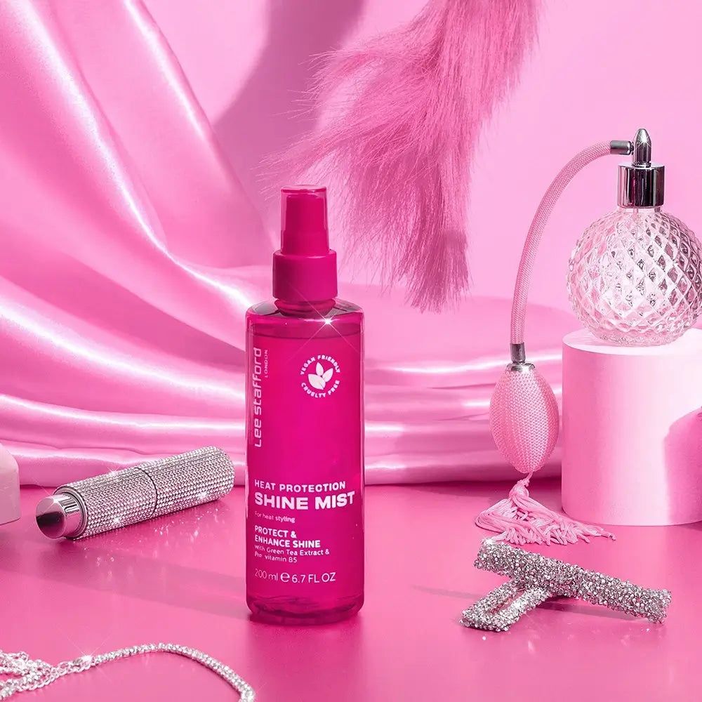 Lee Stafford Heat Protection Shine Mist disposto con elementi decorativi su sfondo rosa.