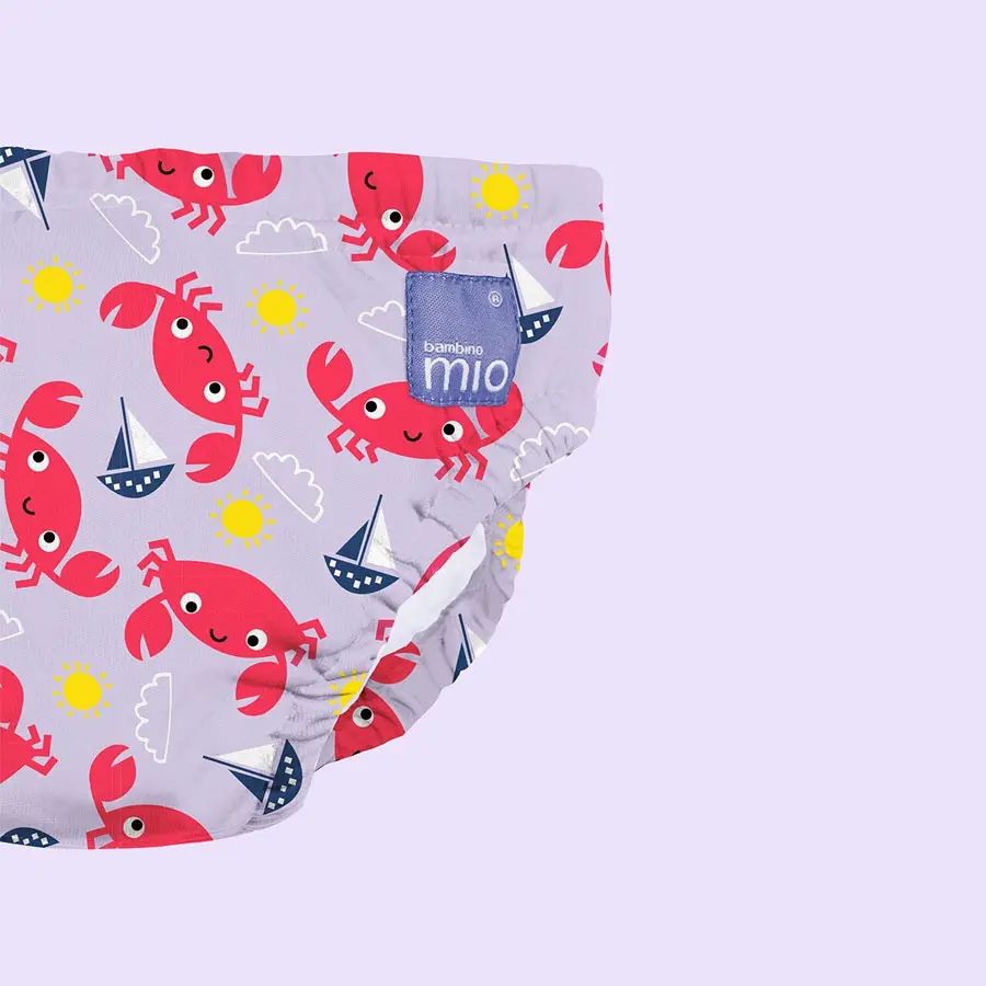 Primo piano del costumino con motivo a granchio. Tessuto viola con granchi, barche a vela e soli.