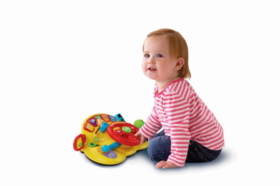 Bambino piccolo seduto che gioca con un volante giocattolo giallo. Il bambino indossa una maglietta a righe rosse e bianche.