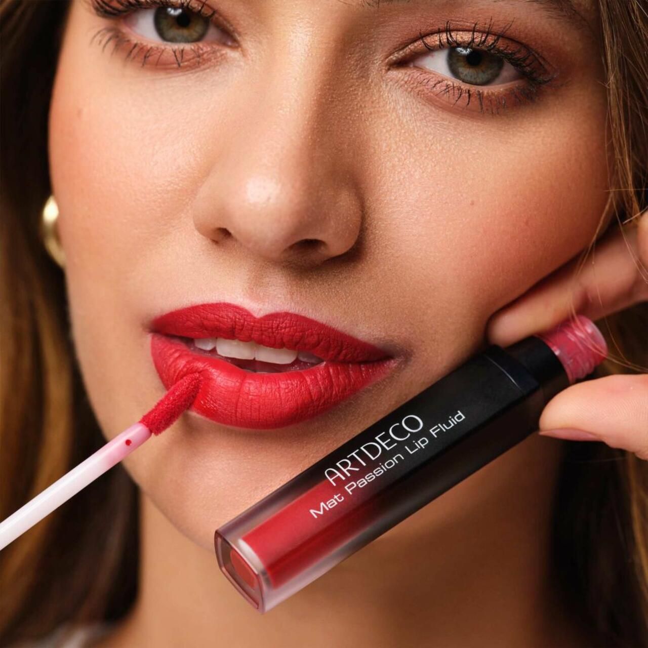 Donna applica lip fluid rosso. Flacone con scritta: ARTDECO Mat Passion Lip Fluid. Applicatore visibile.