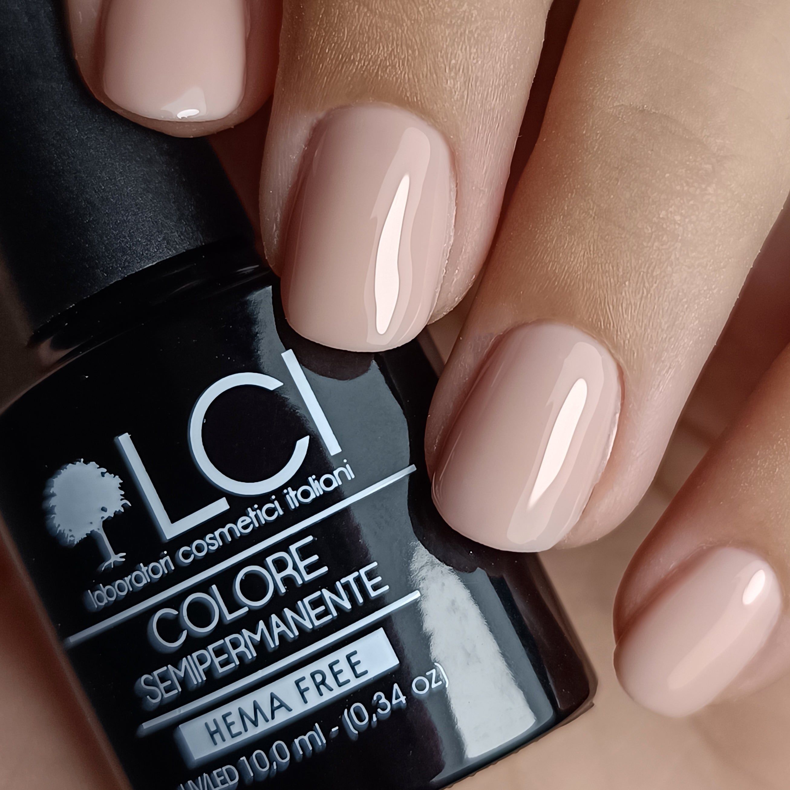 Mano con unghie smaltate e flacone di smalto. Unghie smaltate beige chiaro. Flacone con tappo nero ed etichetta.
