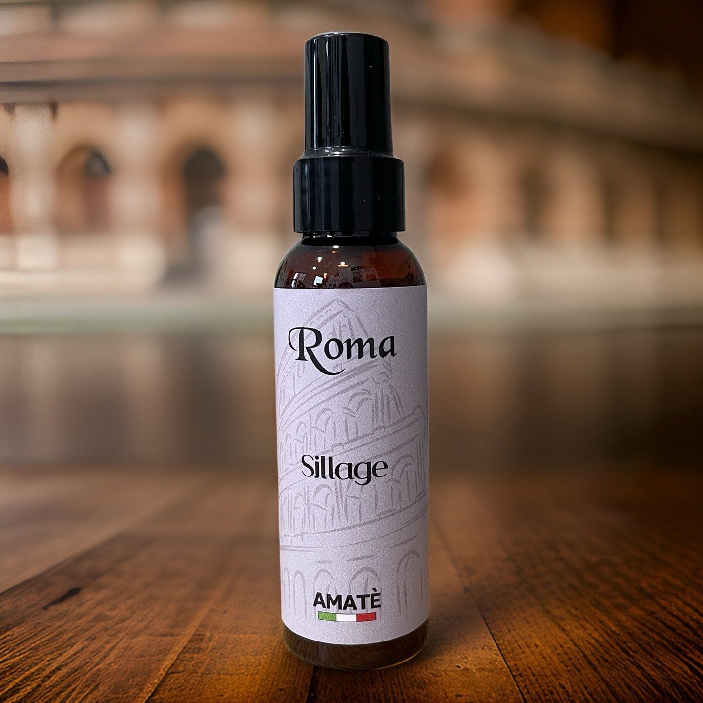 Flacone marrone con vaporizzatore nero su legno. Scritta "Roma Sillage" e "AMATÈ".