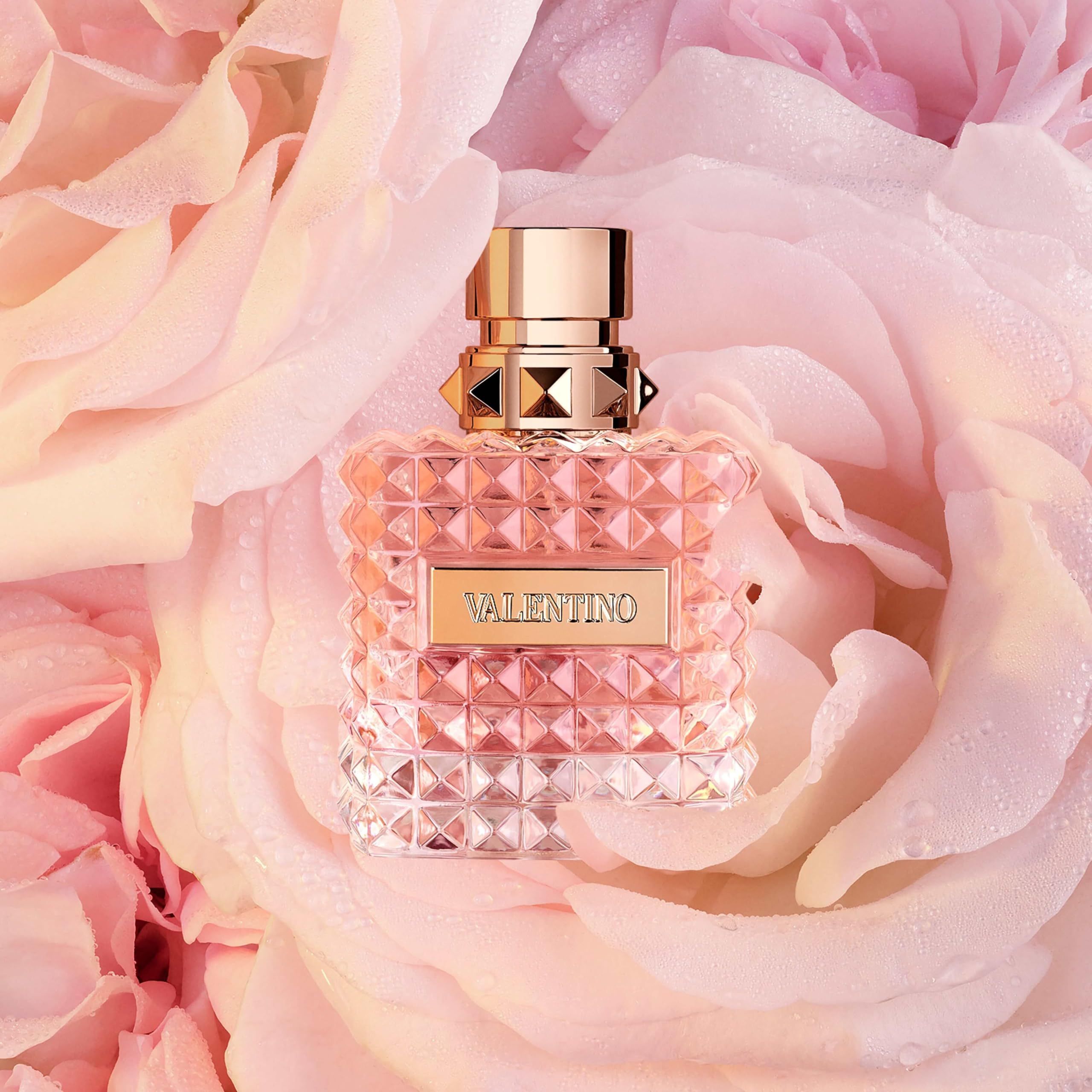Flacone di profumo su petali di rosa. Tappo dorato, vetro sfaccettato quadrato. Scritta: VALENTINO.