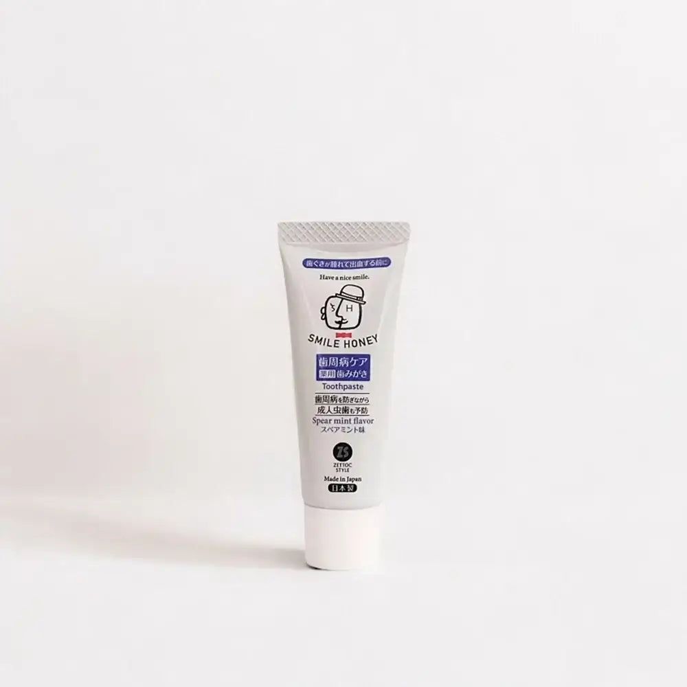 Tubo di dentifricio "SMILE HONEY". Tubo grigio, tappo bianco. "Spear mint flavor" visibile.