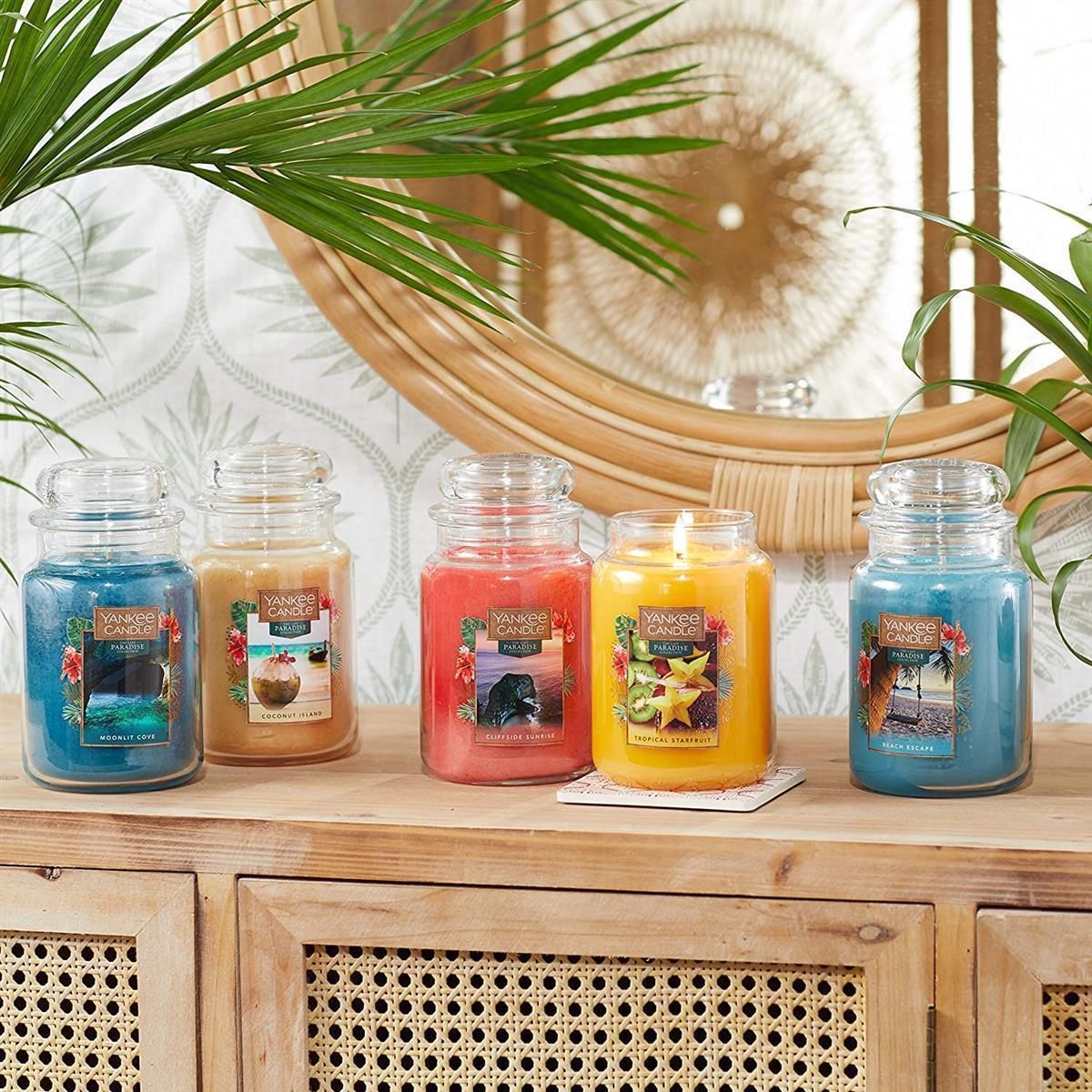 Cinque candele profumate Yankee Candle su superficie in legno. Diversi colori e profumi. Etichette con immagini e testo.