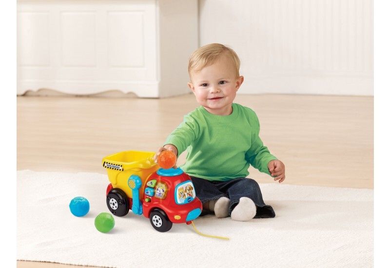 Bambino seduto che gioca con un autocarro ribaltabile giallo e rosso e palline colorate. Cassone giallo, cabina rossa.