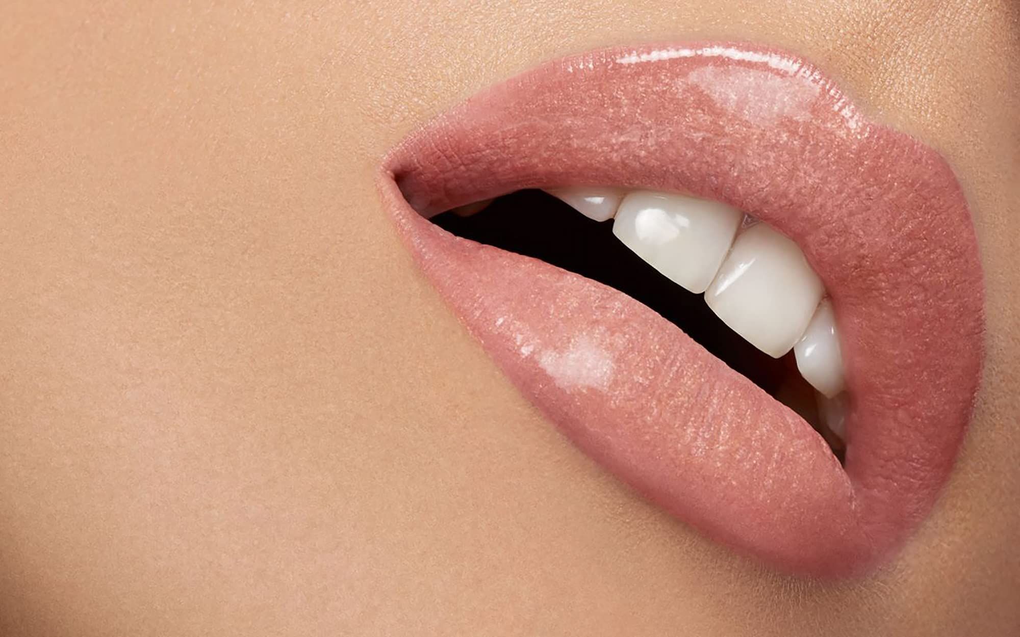 Primo piano di labbra con rossetto rosa. Bocca aperta, denti visibili. Pelle sullo sfondo.