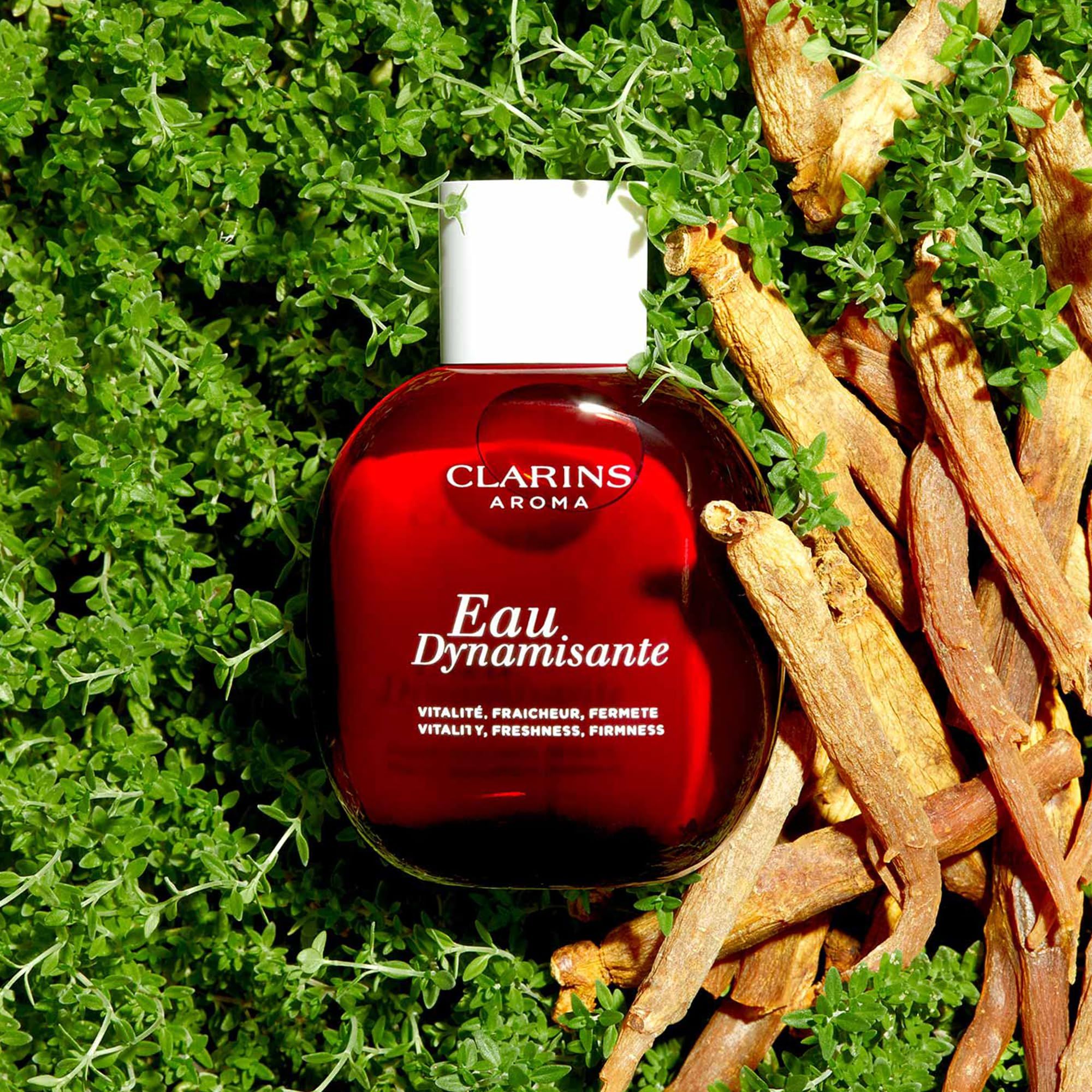 Flacone rosso, tappo bianco, circondato da erbe e radici. Scritta: Clarins Aroma, Eau Dynamisante.