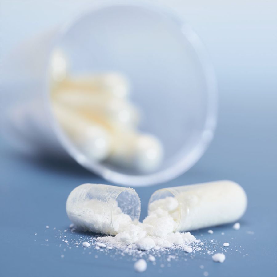 Capsula trasparente aperta con polvere bianca. Altre capsule accanto. Sfondo blu.