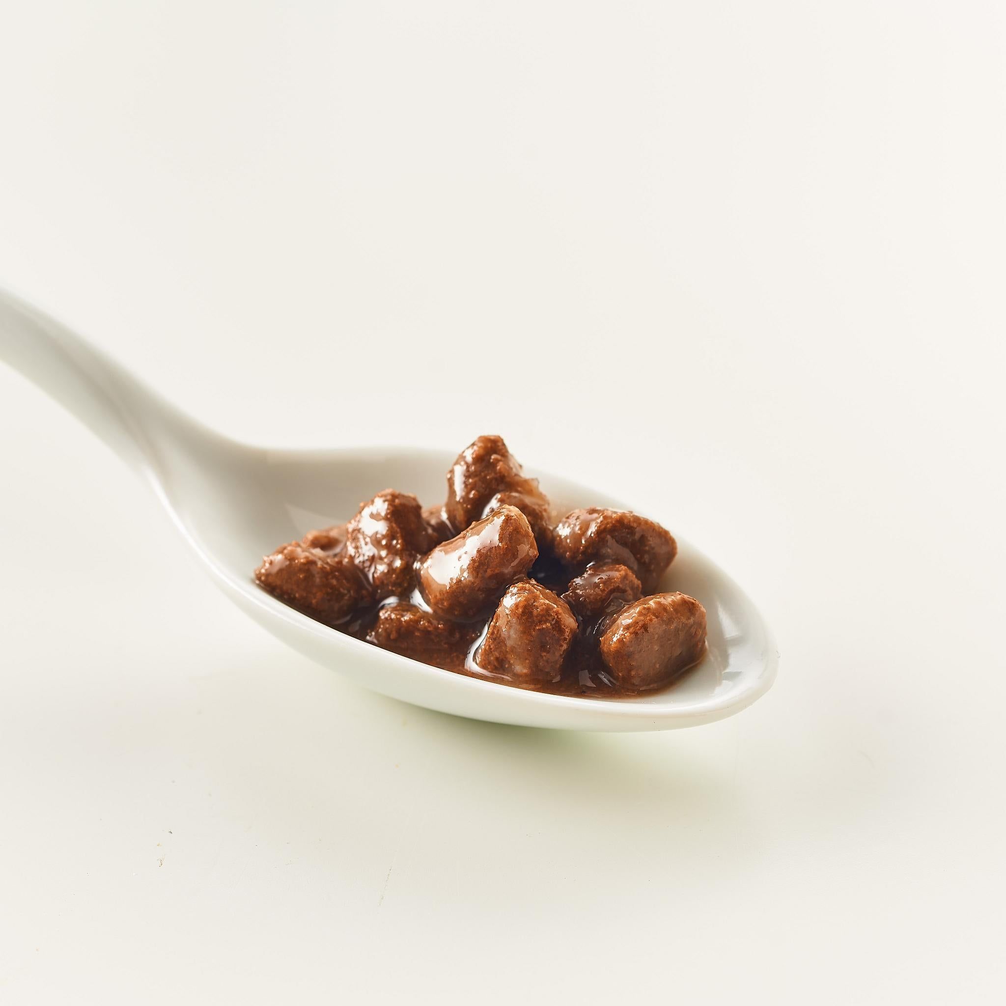Cucchiaio con crocchette marroni. Sfondo bianco.