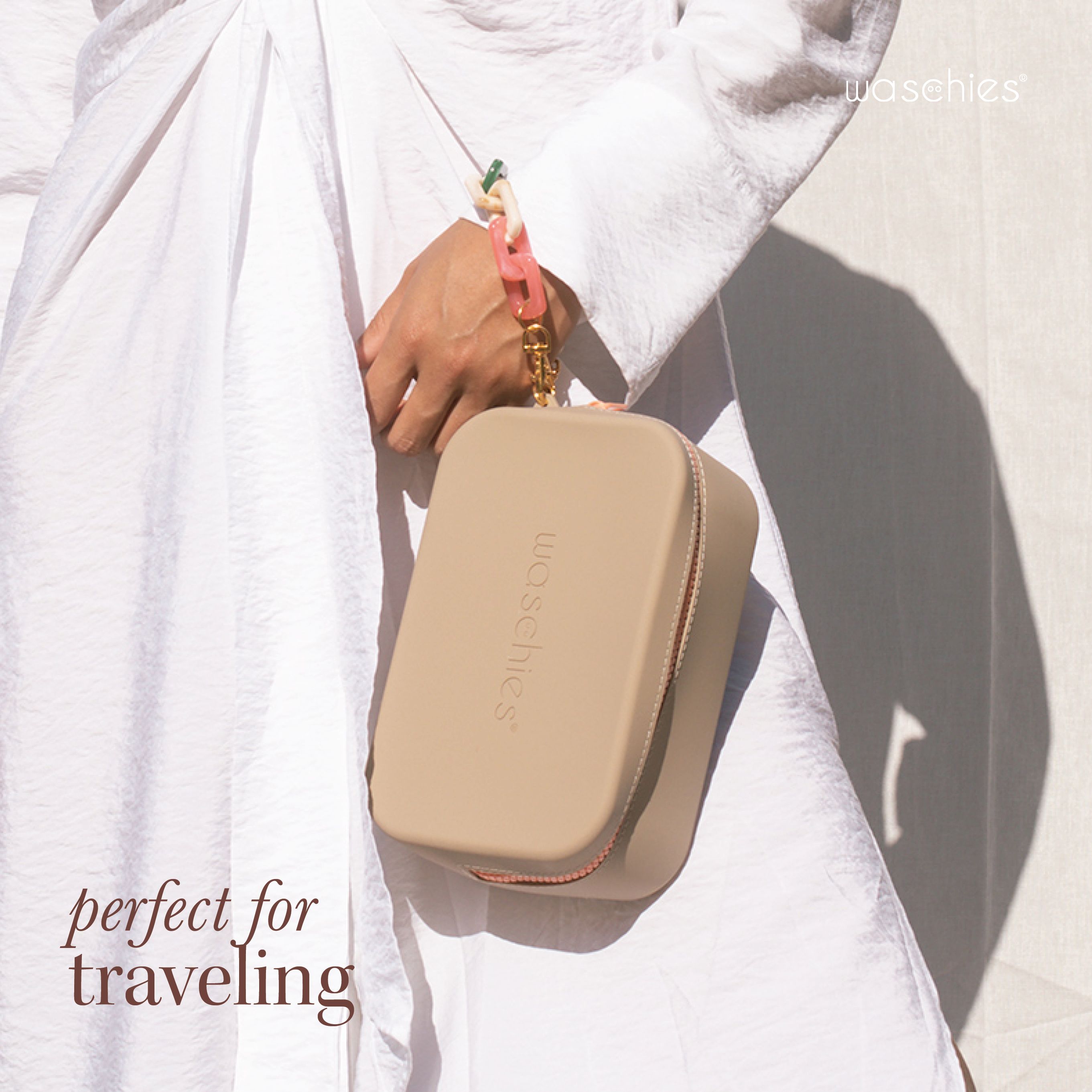 Persona che tiene in mano una pochette cosmetica beige con cerniera e ciondolo. "waschies" è scritto sulla borsa.