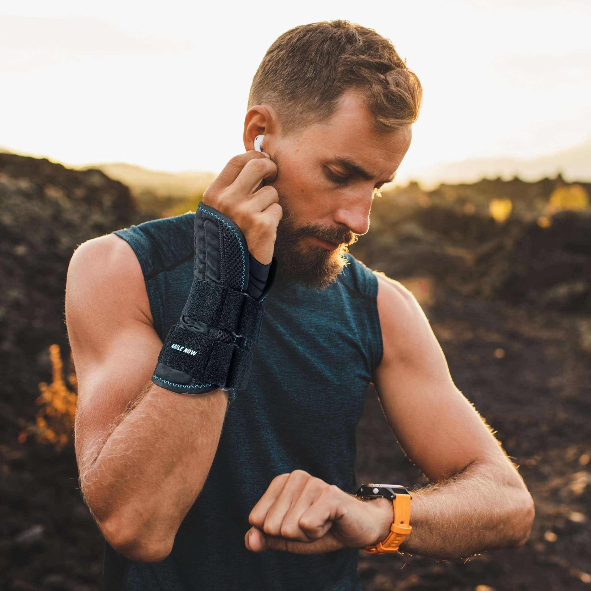Uomo con tutore per polso. Nero, con velcro. Testo: AGILE NOW. Indossa cuffie e smartwatch. All'aperto.