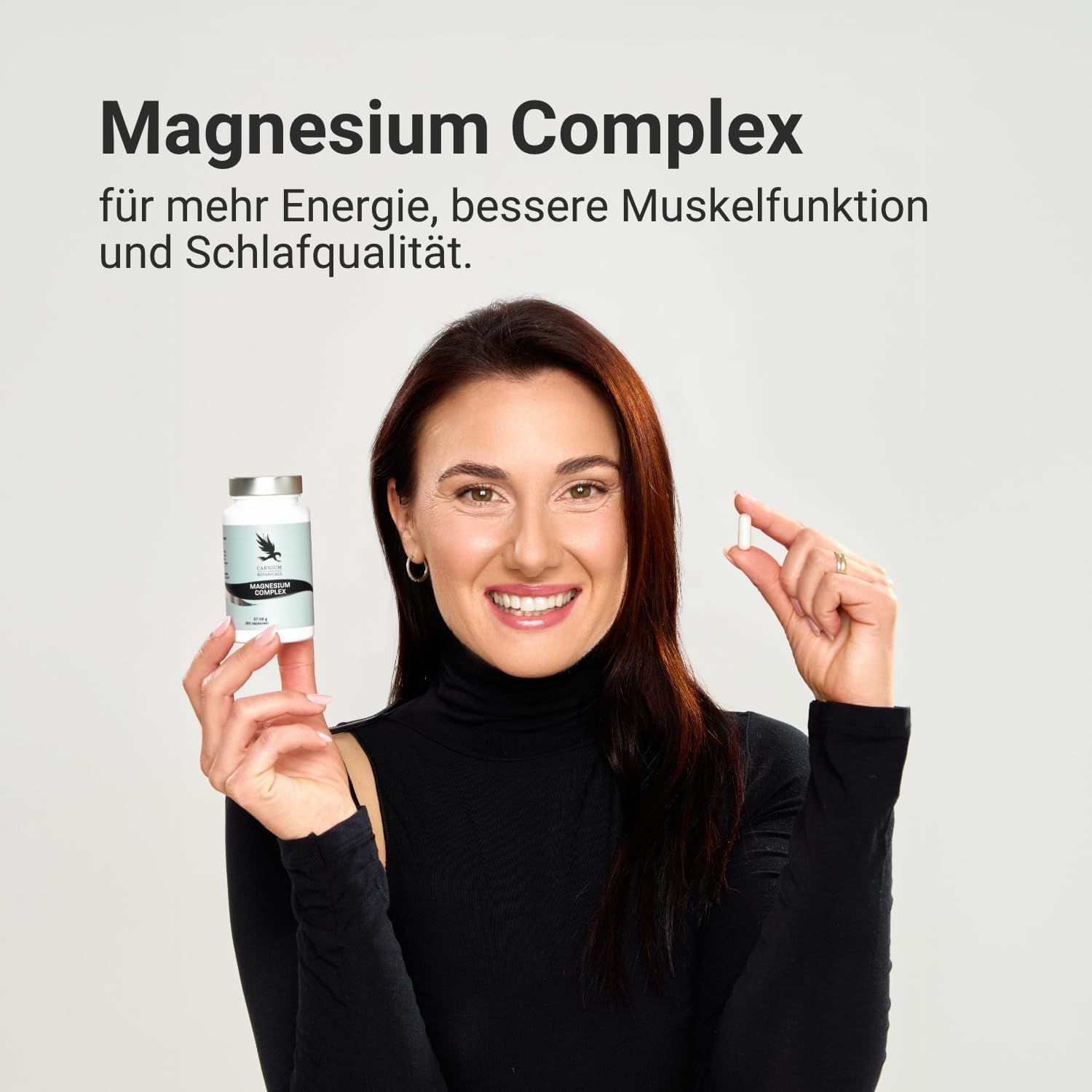 Donna tiene una capsula. Flacone CARNIUM BOTANICALS Magnesium Complex. Testo: Per più energia, migliore funzione muscolare e qualità del sonno.