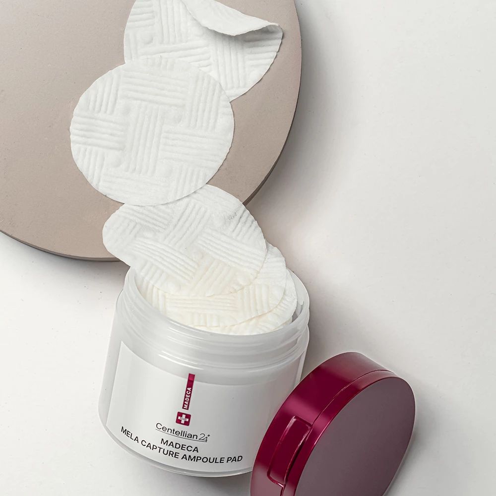 Barattolo bianco aperto con coperchio rosso. Pad rotondi all'interno e accanto. Nome del prodotto e marchio stampati.