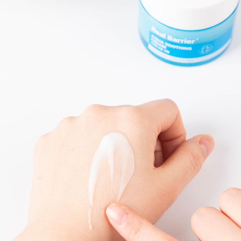 Mano con crema. Un dito tocca la crema. Nome del prodotto non visibile.