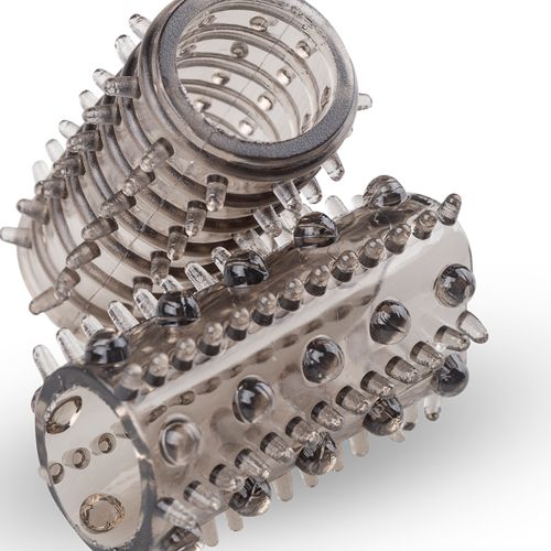 Primo piano di un rivestimento penieno in silicone trasparente con borchie e un anello. Su sfondo bianco.