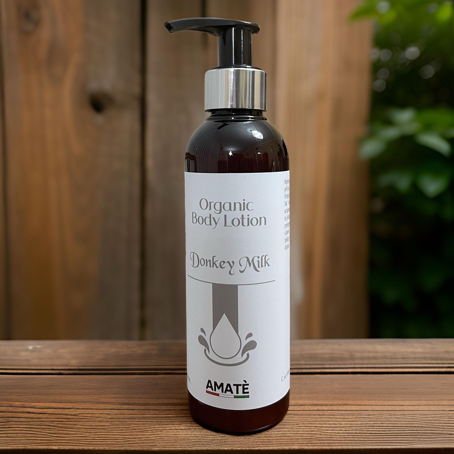 Flacone marrone con dosatore su superficie in legno. Scritta: Organic Body Lotion Donkey Milk. Marchio: AMATÈ.