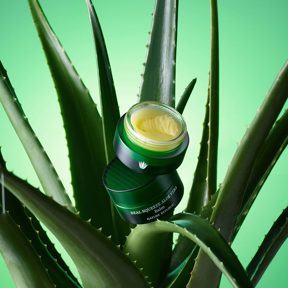 Vasetto verde con balsamo giallo su foglie di aloe vera. Scritta: Real Squeeze Aloe Vera Balm.