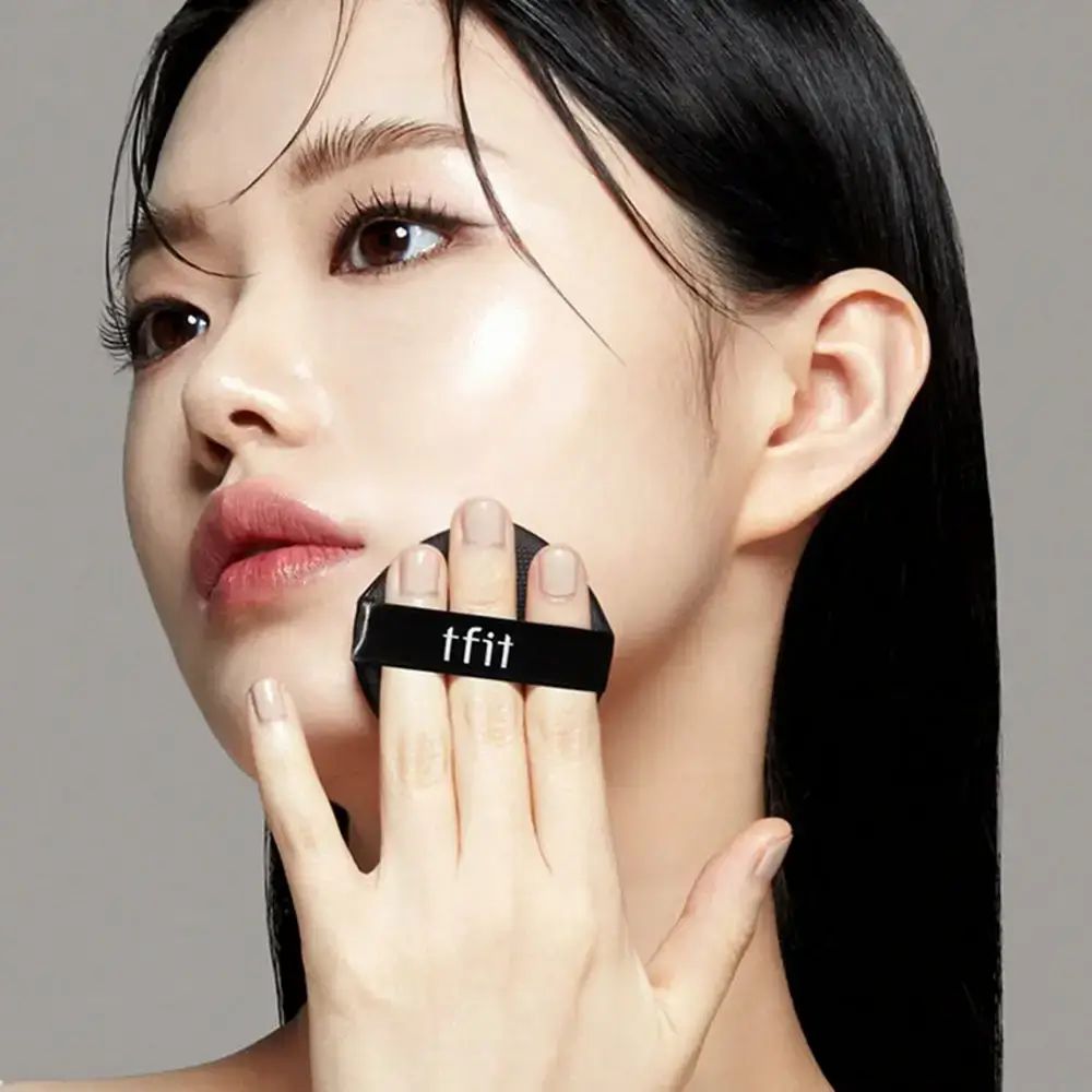 Persona con spugnetta per trucco. Spugna nera con scritta "tfit". Applicazione fondotinta.