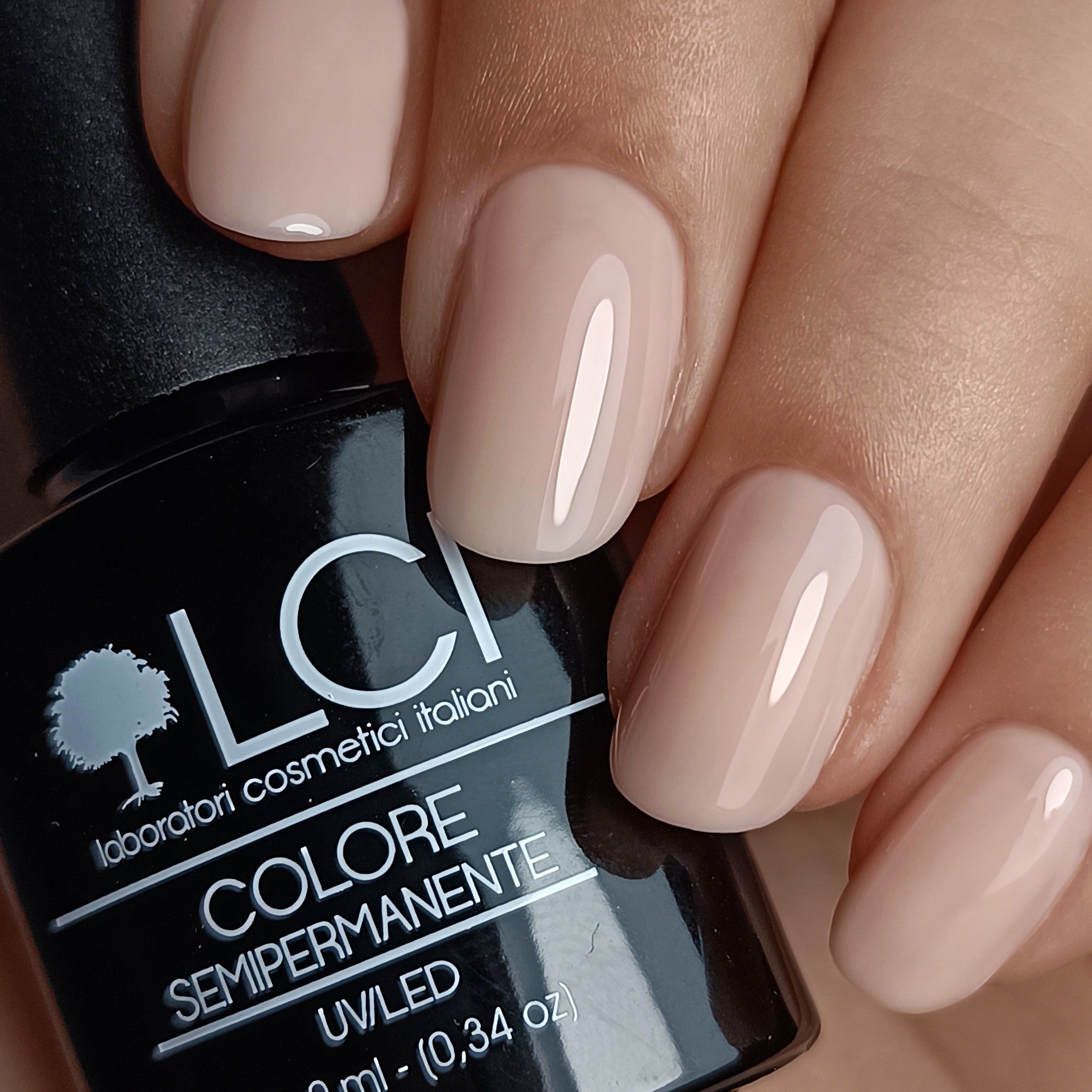 Unghie smaltate Nude ALMOND. Flacone smalto nero sullo sfondo. Mano con unghie smaltate.