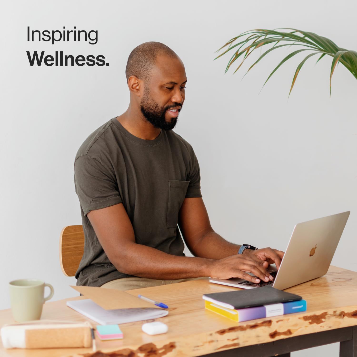 Uomo seduto a una scrivania con un laptop. Sul tavolo: quaderni, tazza, penna. Inspiring Wellness.