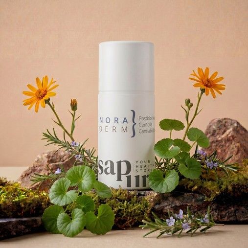 Flacone dispenser bianco con loghi 'Nora Derm' e 'SAPURA', circondato da muschio, pietre e fiori gialli.