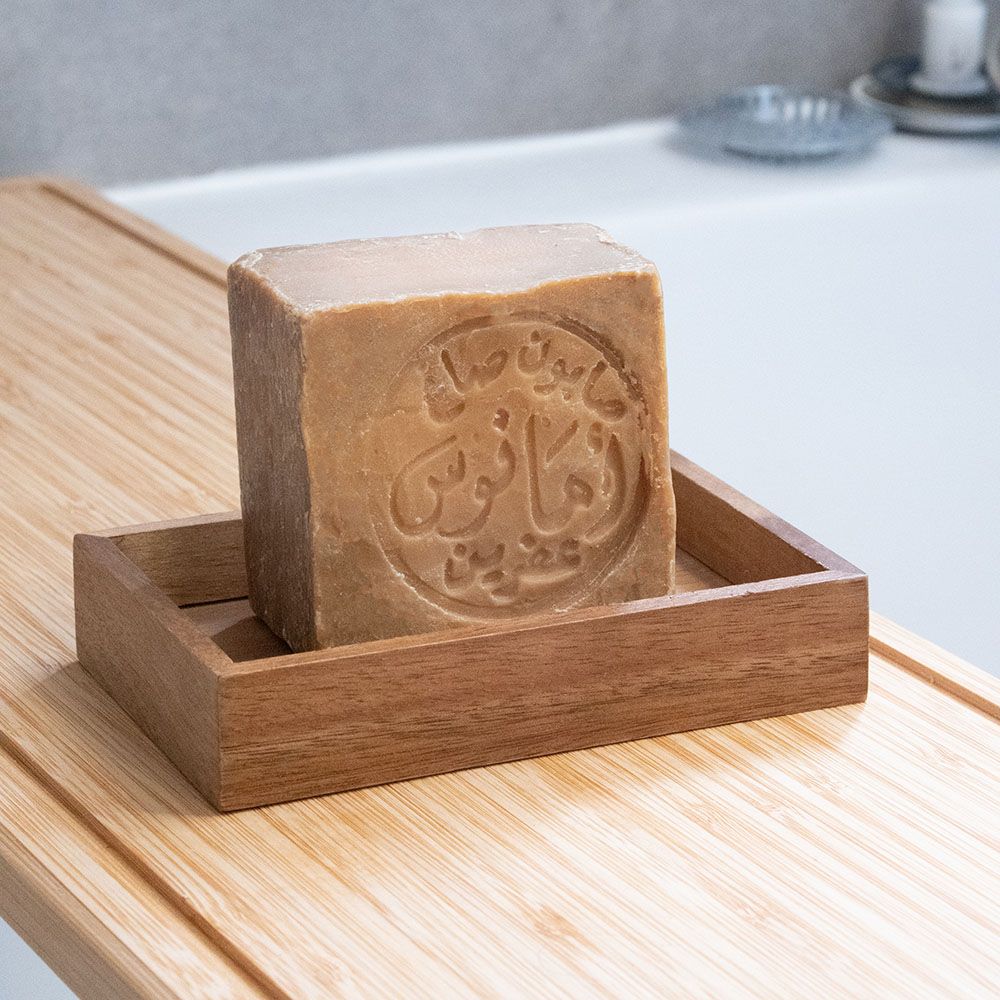 Un sapone quadrato, caratteri arabi, in un portasapone di legno. Su tavola di legno.