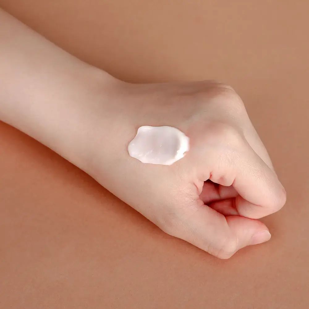 Mano con una macchia di crema. La crema è bianca. Lo sfondo è marrone.